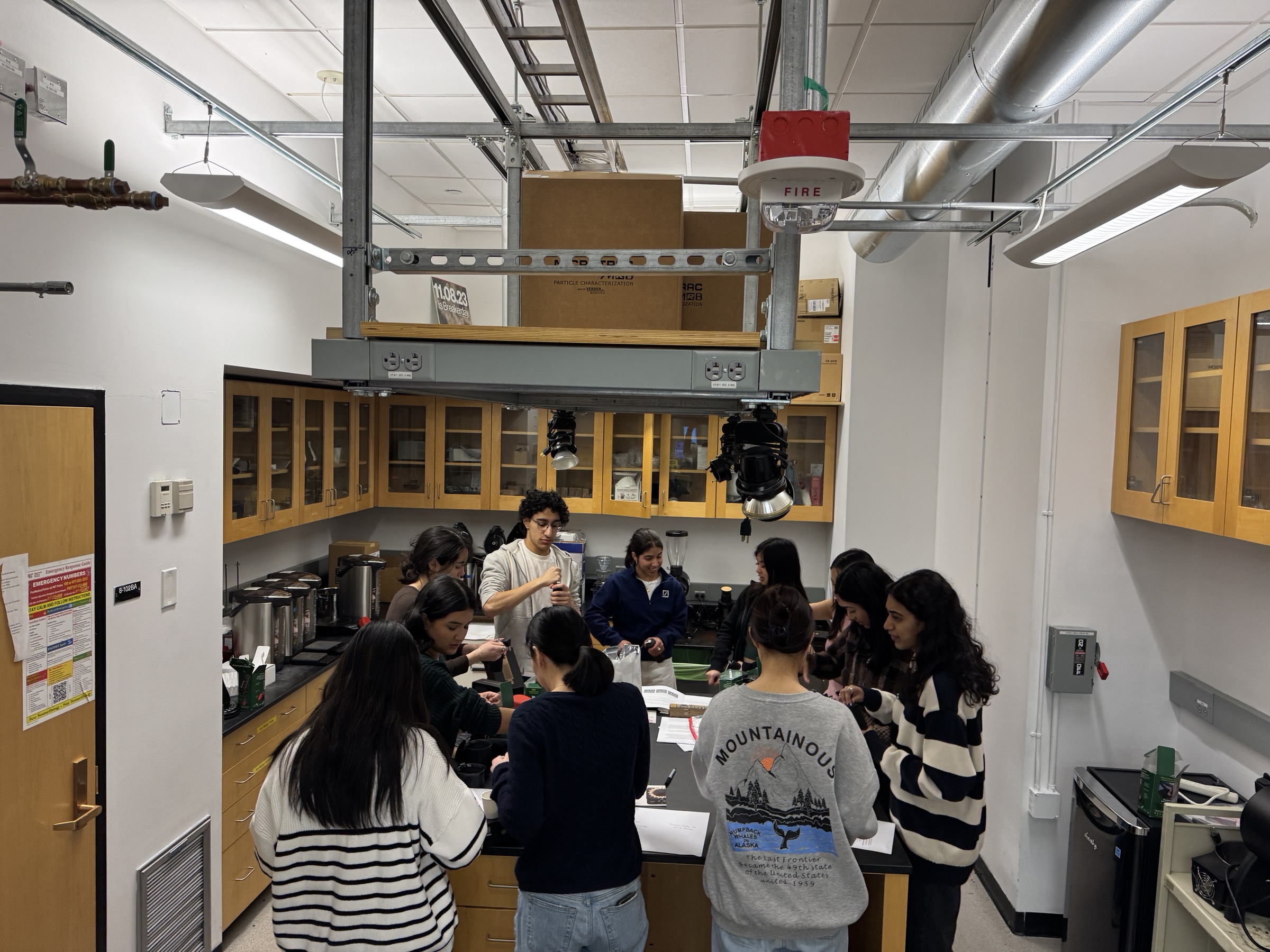A second 3.000 cohort preparing coffee together around the central workbench in food-safe room 8-102B.