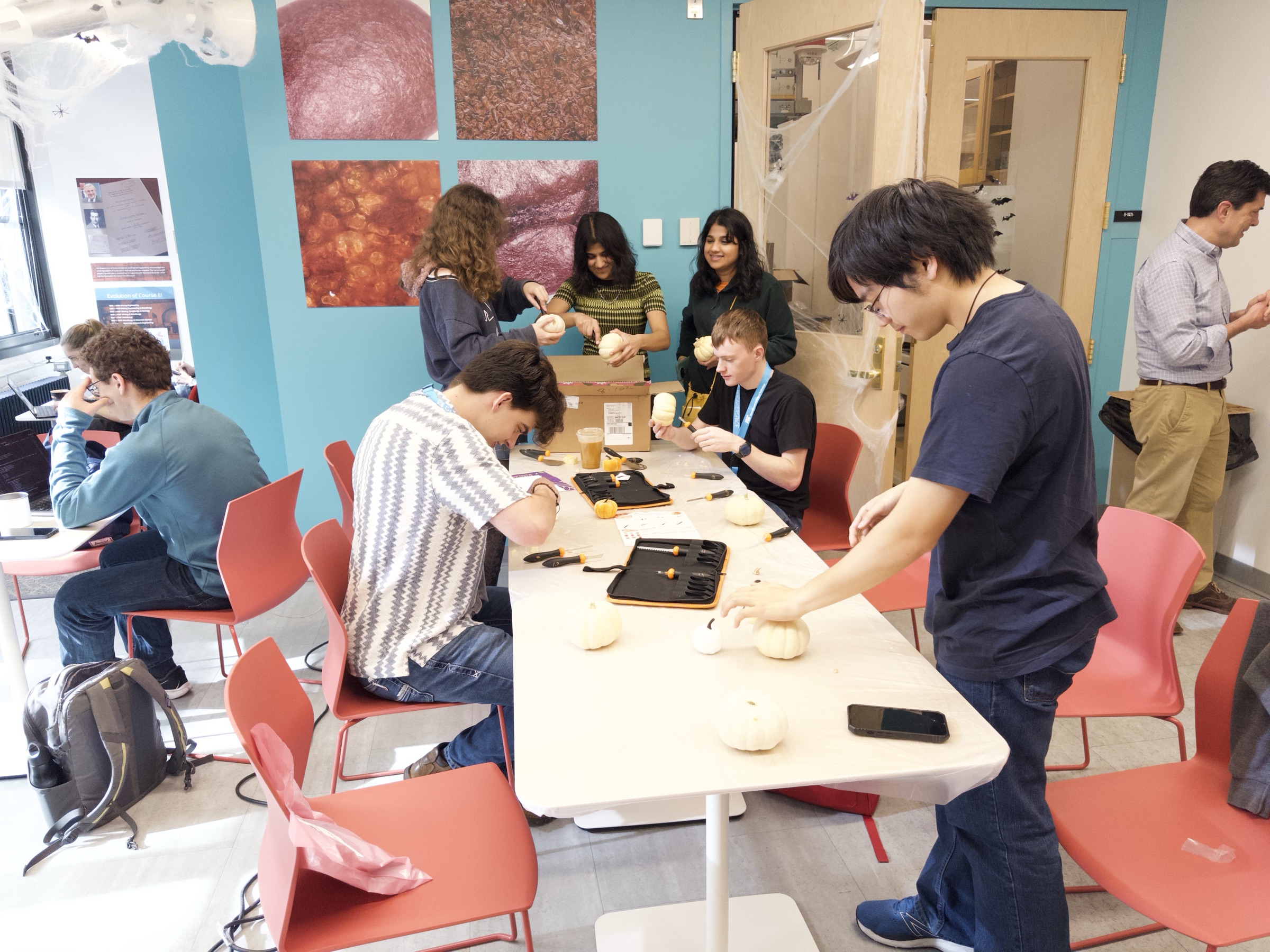 Students carving small pumpkins at shared tables in the Breakerspace Lounge during Infinite Halloween.