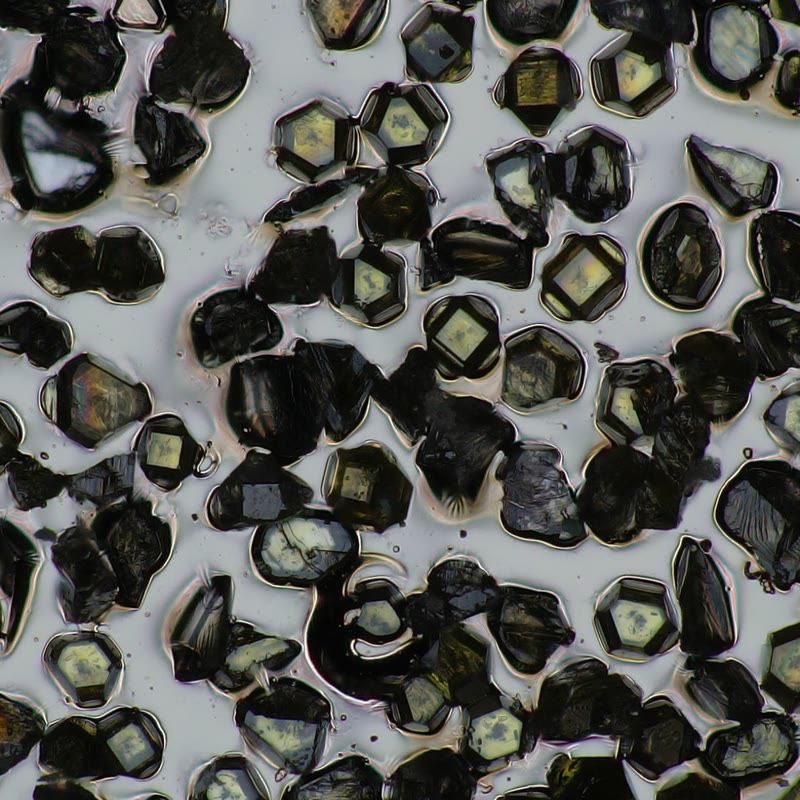 Reflected-light microscope view showing many angular, faceted diamond grains embedded in a pale metallic matrix.