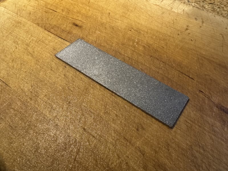 Rectangular diamond sharpening stone resting diagonally on a worn wooden cutting board.